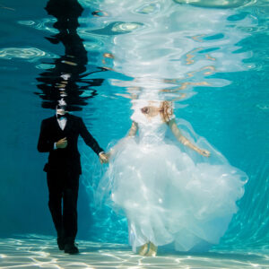 A couple is photographed in their wedding attire from underwater