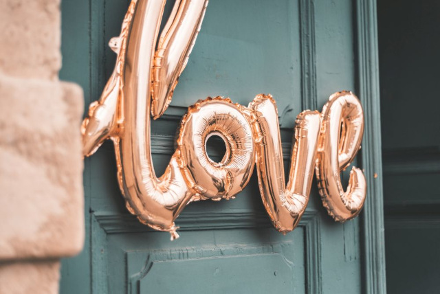 Vor einer blaugrünen Tür prangen goldene Folienballons mit der Aufschrift „Love“, die dem eleganten Glanz der Ballons einen rustikalen Charme verleihen.
